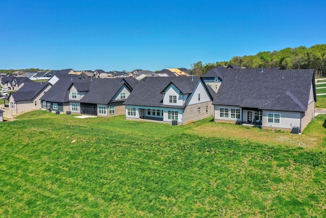 rear view of property with a yard, central AC unit, a residential view, and roof with shingles