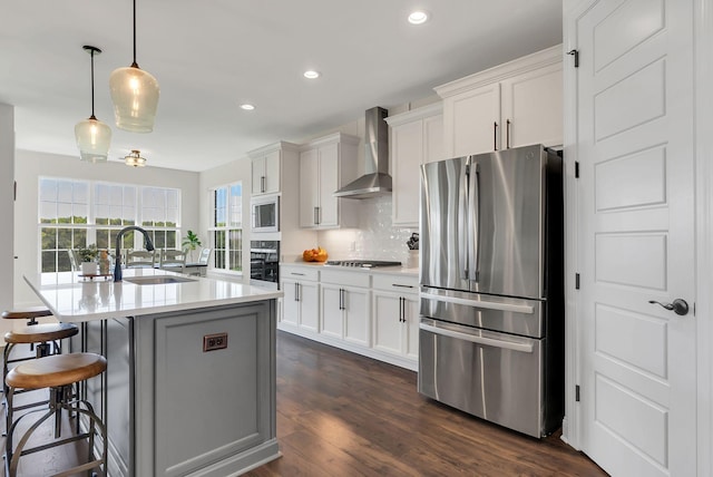 kitchen featuring wall chimney exhaust hood, a sink, appliances with stainless steel finishes, dark wood-style floors, and backsplash