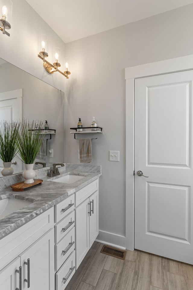 full bath with visible vents, baseboards, a sink, double vanity, and wood finished floors