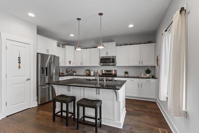 kitchen with white cabinets, a sink, a breakfast bar, dark wood finished floors, and stainless steel appliances