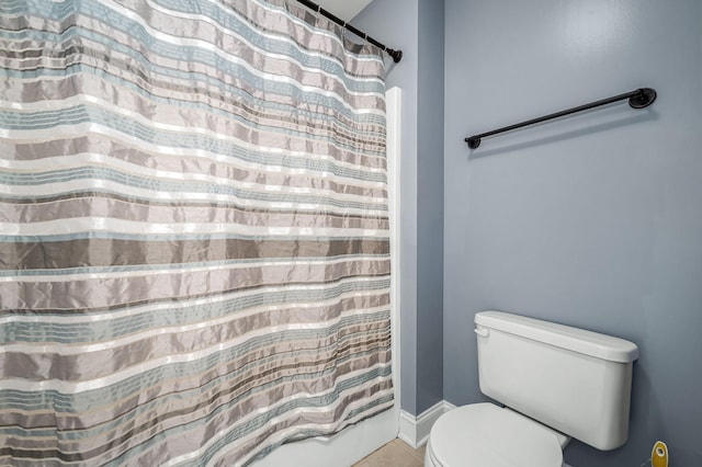 bathroom with toilet, a shower with shower curtain, and baseboards
