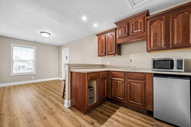 kitchen featuring a sink, light countertops, light wood-type flooring, stainless steel microwave, and fridge