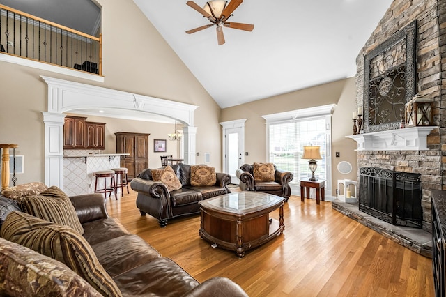 living area featuring a ceiling fan, arched walkways, a brick fireplace, and light wood finished floors
