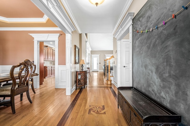 hall with ornamental molding, a wainscoted wall, light wood-type flooring, and ornate columns