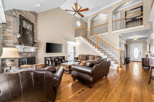 living area with ceiling fan, wood-type flooring, a stone fireplace, and stairway