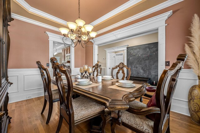 dining area with a notable chandelier, crown molding, a wainscoted wall, and wood finished floors