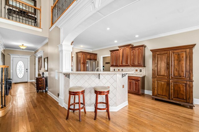 kitchen with light countertops, light wood-type flooring, freestanding refrigerator, a kitchen breakfast bar, and decorative columns