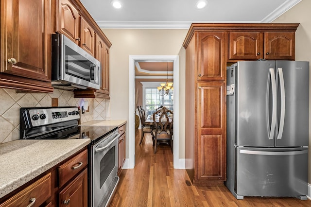 kitchen featuring tasteful backsplash, a chandelier, crown molding, light wood finished floors, and stainless steel appliances