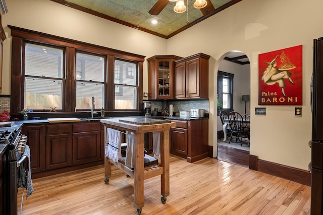 kitchen with tasteful backsplash, high end range, dark countertops, arched walkways, and a sink
