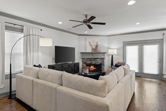 living room featuring ornamental molding, a ceiling fan, a stone fireplace, recessed lighting, and dark wood-style floors