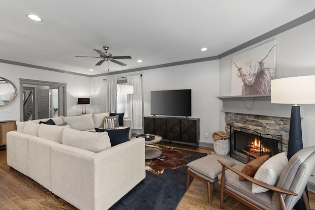 living room featuring crown molding, ceiling fan, a stone fireplace, and wood finished floors