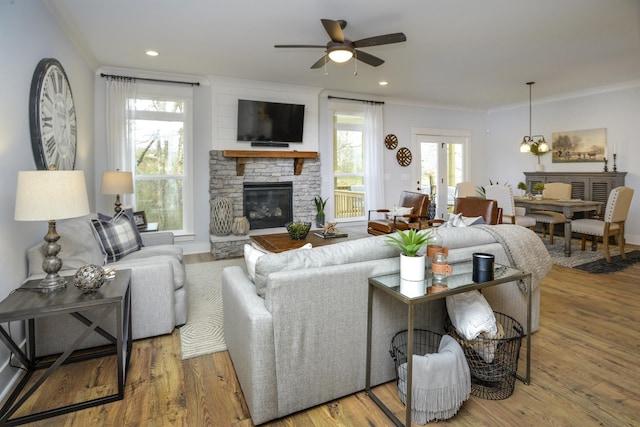 living area with ceiling fan, a stone fireplace, crown molding, and wood finished floors