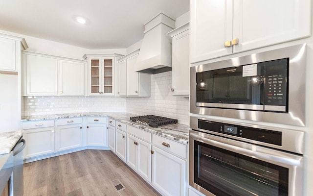 7705 Pine St, Fairview, TN 37062 - kitchen featuring appliances with stainless steel finishes, custom range hood, white cabinetry, and light stone countertops