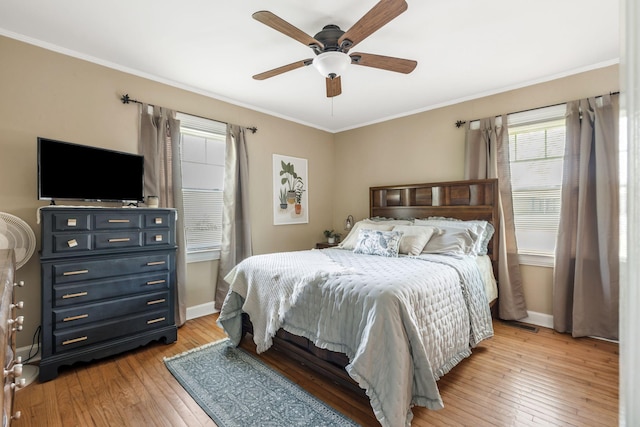 bedroom with ornamental molding, light wood finished floors, baseboards, and multiple windows