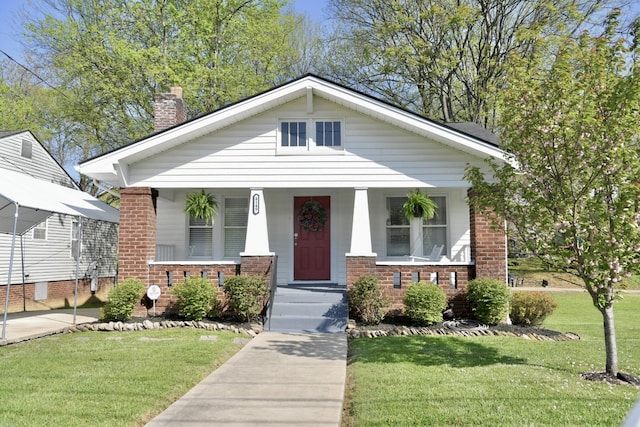 bungalow-style home featuring brick siding, a chimney, a front lawn, and a porch