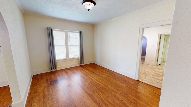 unfurnished room with baseboards, arched walkways, ornamental molding, a textured ceiling, and wood finished floors