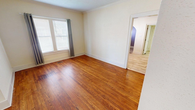 empty room featuring visible vents, baseboards, arched walkways, ornamental molding, and wood finished floors