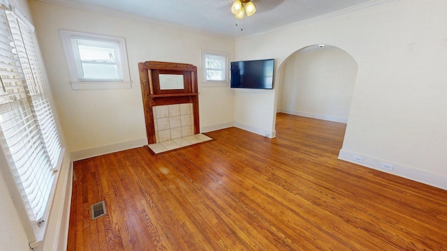 spare room with crown molding, a ceiling fan, visible vents, arched walkways, and wood finished floors