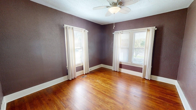 empty room with light wood finished floors, a textured wall, visible vents, a ceiling fan, and baseboards