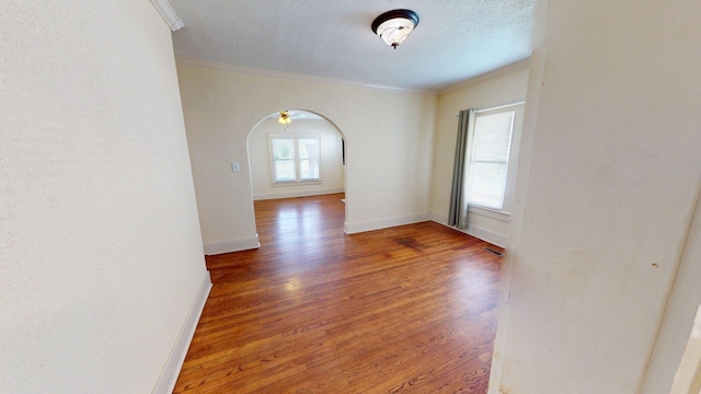 empty room with baseboards, crown molding, visible vents, arched walkways, and wood finished floors
