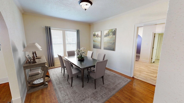 dining area featuring baseboards, wood finished floors, a textured ceiling, and crown molding