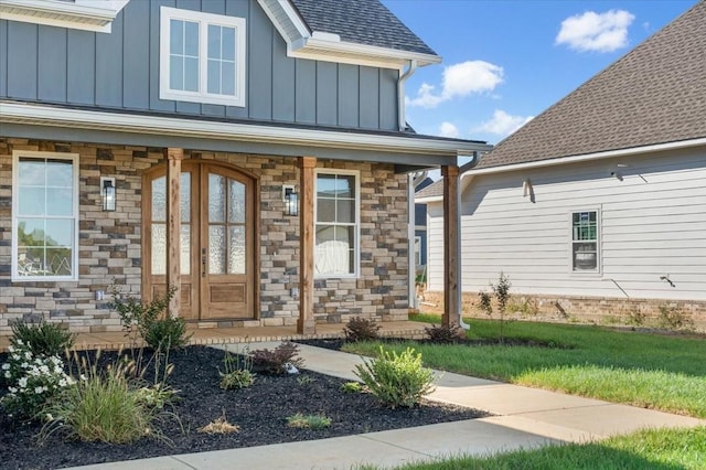 doorway to property with board and batten siding, stone siding, a porch, a yard, and a shingled roof