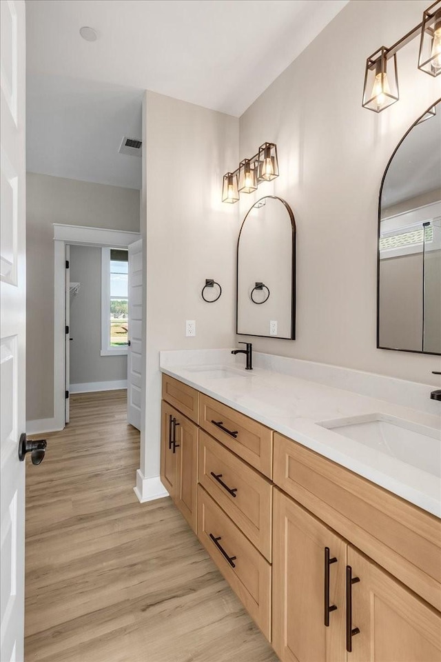 full bath featuring a sink, visible vents, double vanity, and wood finished floors