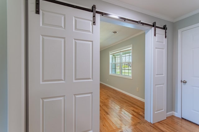 hall with light wood-style flooring, baseboards, ornamental molding, and a barn door