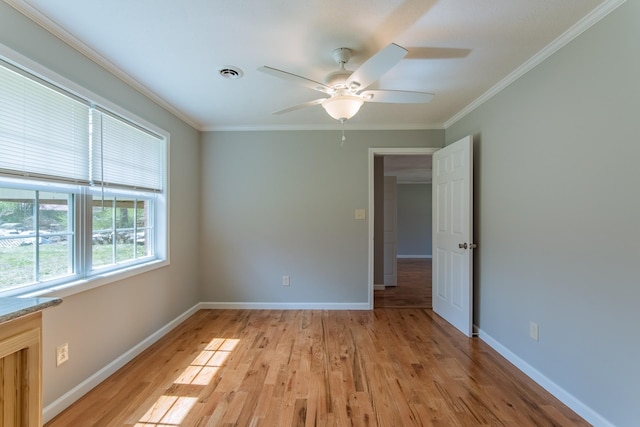 empty room featuring visible vents, baseboards, a ceiling fan, crown molding, and light wood-style flooring