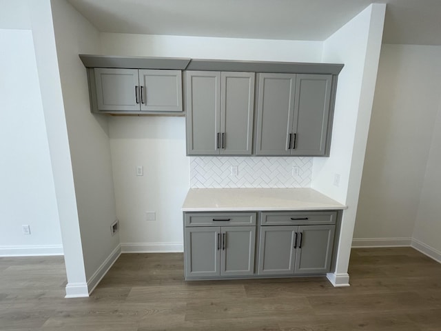 kitchen with backsplash, baseboards, gray cabinetry, and wood finished floors