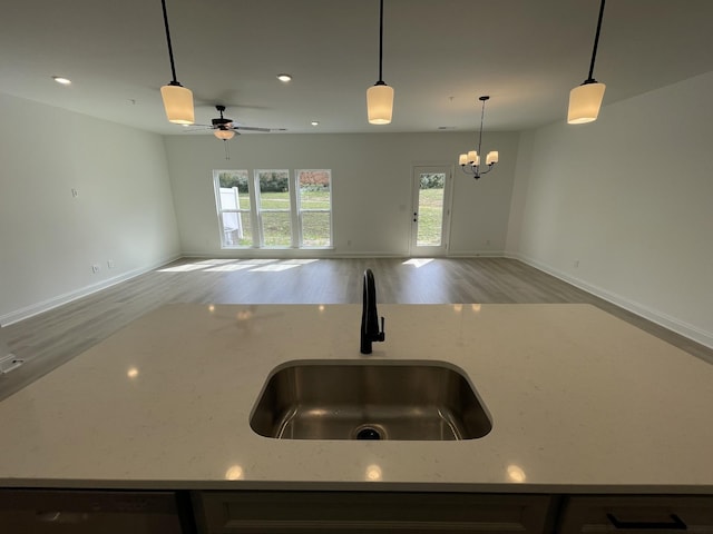 kitchen featuring open floor plan, light stone countertops, pendant lighting, ceiling fan with notable chandelier, and a sink