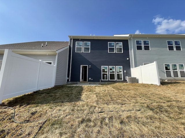 rear view of property featuring central AC unit, fence, and a lawn
