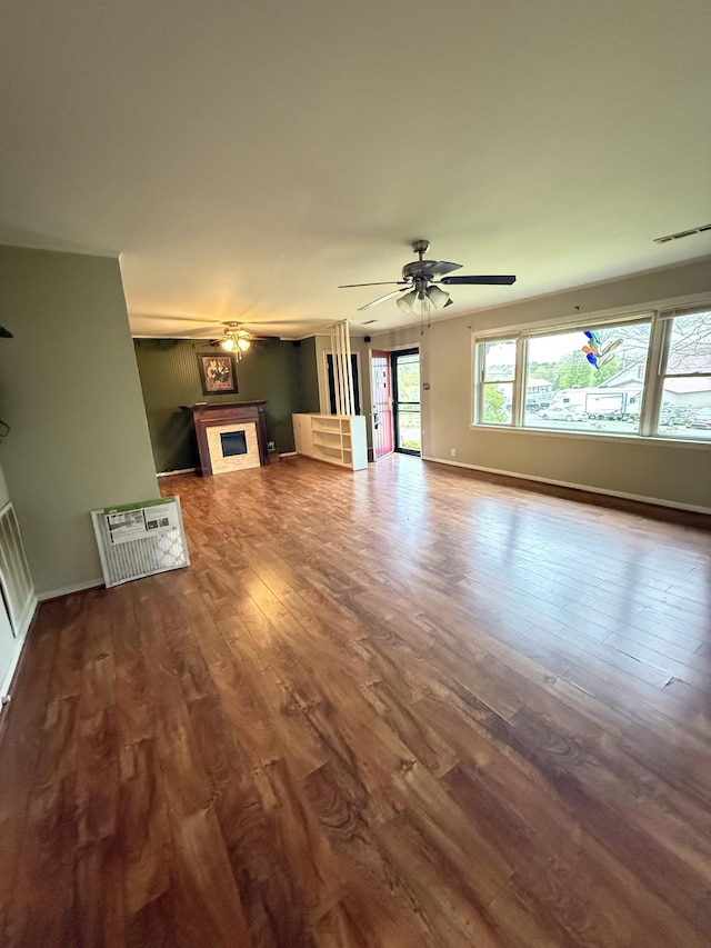 unfurnished living room featuring dark wood-style flooring, baseboards, a fireplace, visible vents, and ceiling fan