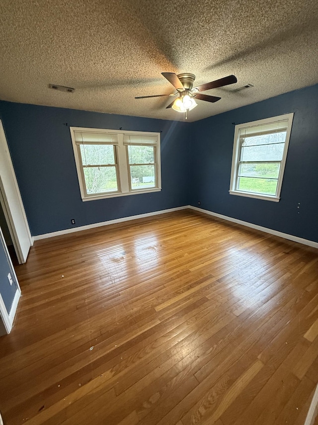 empty room with wood-type flooring, visible vents, and plenty of natural light