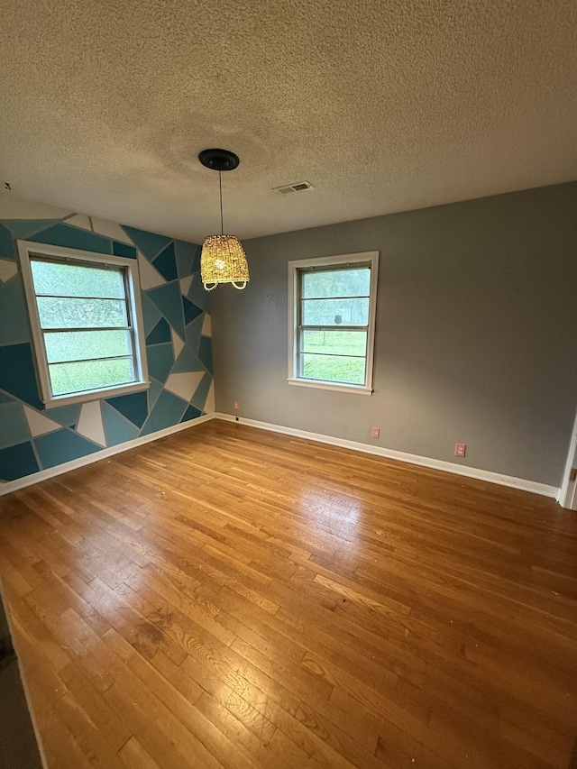 empty room featuring plenty of natural light, visible vents, hardwood / wood-style flooring, and baseboards