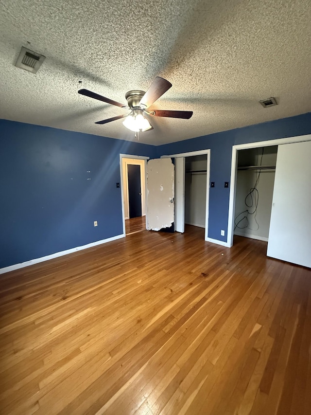 unfurnished bedroom with visible vents, multiple closets, hardwood / wood-style flooring, and baseboards