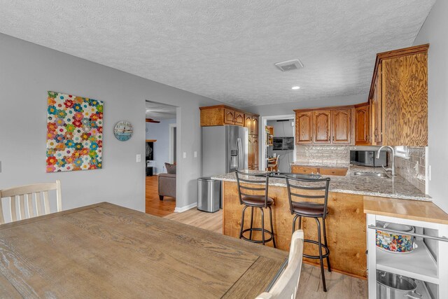 211 Northview Ct, Hendersonville, TN 37075 - kitchen featuring appliances with stainless steel finishes, light wood-style floors, a peninsula, brown cabinets, and a textured ceiling