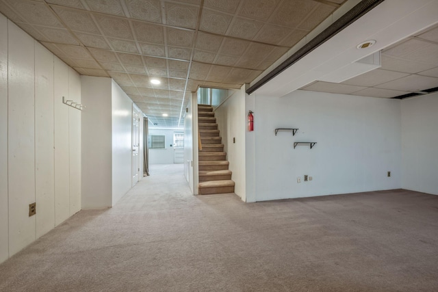 finished below grade area with wooden walls, carpet floors, stairway, and a drop ceiling