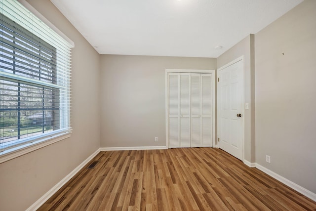 unfurnished bedroom featuring a closet, visible vents, baseboards, and wood finished floors