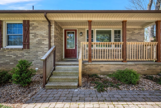 doorway to property with a porch and brick siding