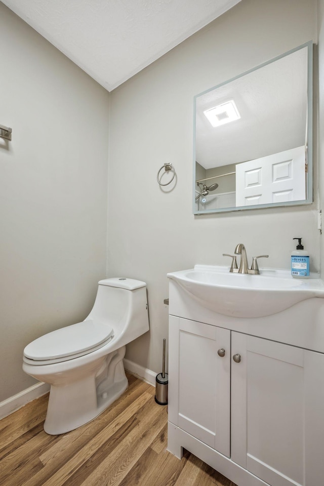 bathroom featuring toilet, vanity, wood finished floors, and baseboards