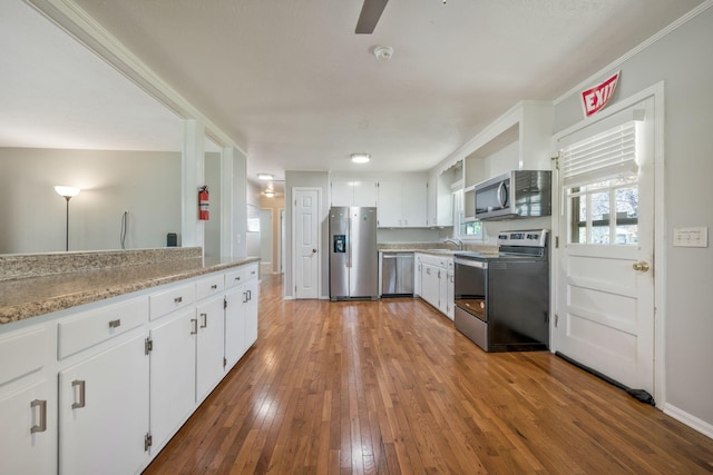 kitchen with a sink, ceiling fan, appliances with stainless steel finishes, white cabinetry, and hardwood / wood-style floors