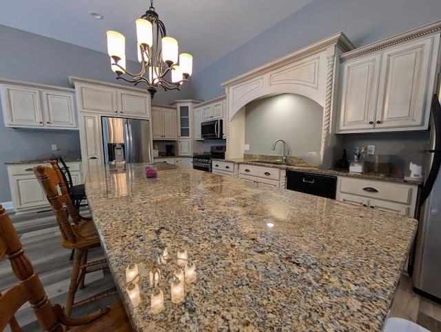kitchen featuring a large island, light stone counters, a sink, stainless steel appliances, and a notable chandelier