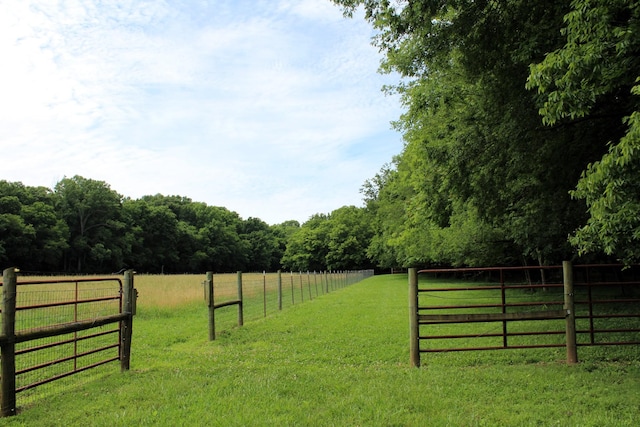 view of yard featuring a rural view, fence, a gate, and a wooded view