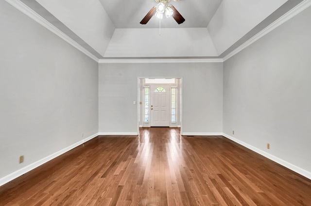 empty room with baseboards, ornamental molding, ceiling fan, a tray ceiling, and wood finished floors