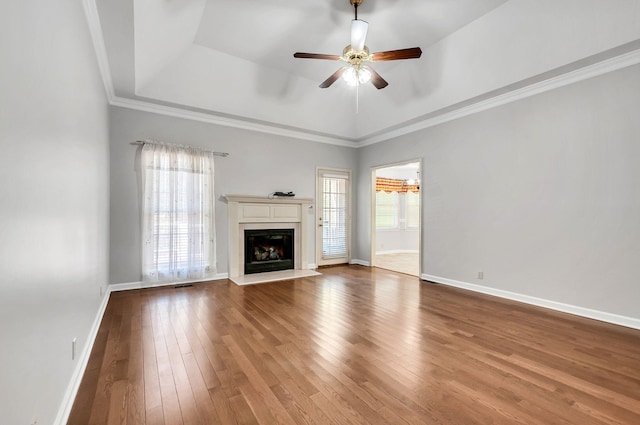 unfurnished living room with baseboards, a fireplace with raised hearth, a tray ceiling, ceiling fan, and wood finished floors