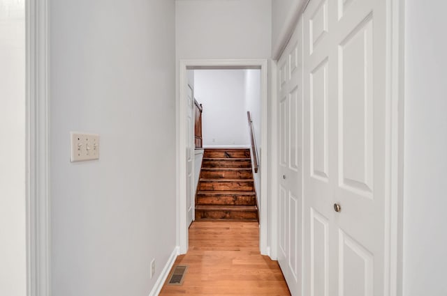 hallway featuring light wood finished floors, baseboards, visible vents, and stairway