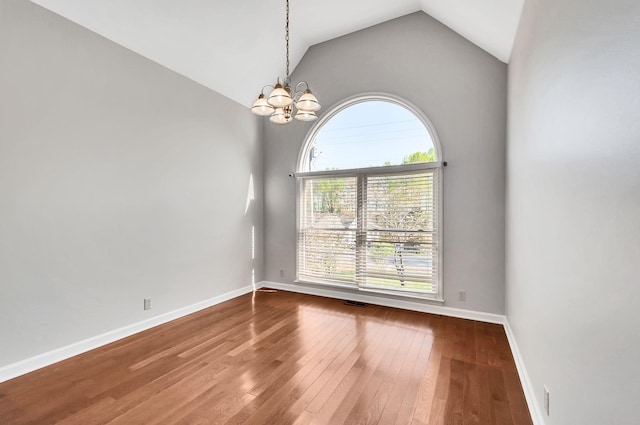 unfurnished room with baseboards, hardwood / wood-style floors, a notable chandelier, and lofted ceiling