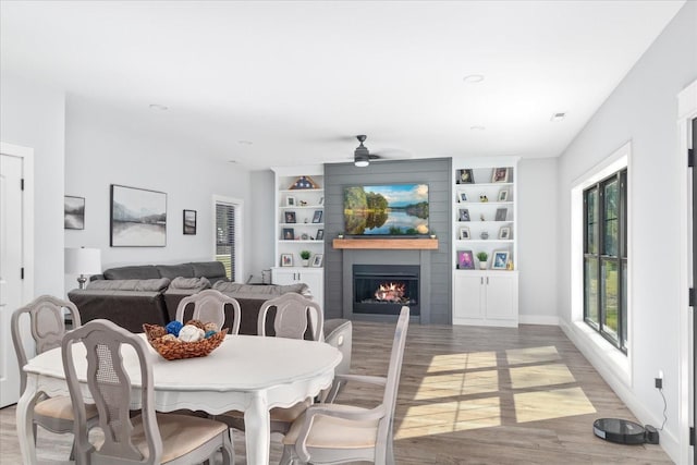 dining area with baseboards, built in features, a large fireplace, ceiling fan, and wood finished floors