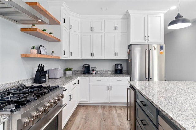 kitchen featuring premium appliances, wall chimney range hood, white cabinetry, light wood-style flooring, and light stone counters